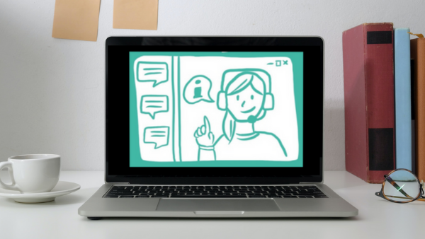 Laptop auf einem Schreibtisch. Auf dem Bildschirm eine Illustration von einer Person mit Headset und gehobenem Zeigefinger. Links neben der Person sind Sprechblasen zu sehen.